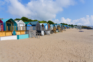 Beach huts of all shapes and sizes line the back of Abersoch beach on a bright summer day.