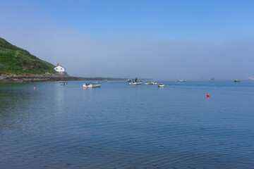 Just outside Porthdinllaen harbour in Wales a thick bank of fog sits under a blue summer sky.