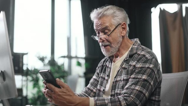 Portrait of excited happy gray haired senior businessman enjoying success reading good news message on smartphone screen in the modern office workplace Triumph Victory Win concept 