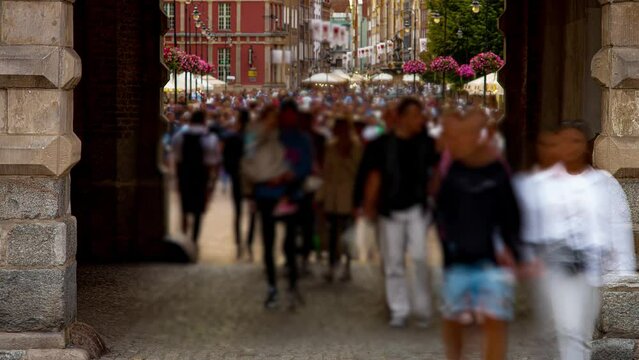Defocused and motion blurred time lapse of crowds of people walking on busy shopping street through vintage arch of building. Vacations and traveling, tourism and tourists concept