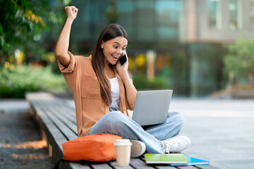 Cheerful woman student engaging in phone call and laptop study
