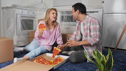 Happy couple eat hot pizza after kitchen renovation end. Family take fast food break. People move into new home. Girl sit floor. Joy guy rent house. Buyer tasty junk meal. Man buy real estate concept.
