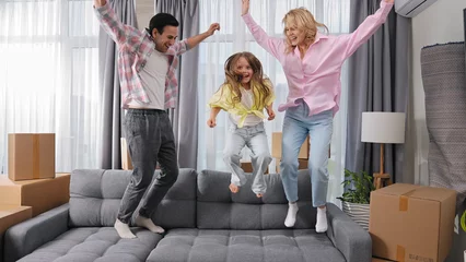 Foto op Aluminium Happy family move into new house. Little girl jump on sofa. Crazy child have fun. Funny dad buy flat. Silly kid play home. Joy mom rest couch. Sale real estate concept. Smiling people rent furniture. © sibway