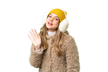 Young girl wearing winter muffs over isolated chroma key background saluting with hand with happy expression
