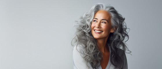 Portrait of a happy smiling beautiful aging mature woman with smooth healthy face skin and long gray hair on white background