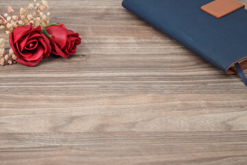 Red roses on the wooden table with a notebook at the side. Copy space for text, messages, advertisements, etc.