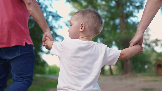 happy family in the park. a child walks with his parents holding hands, view from back in park in nature, walking. happy family kid dream concept. child son walking sun with parents in park