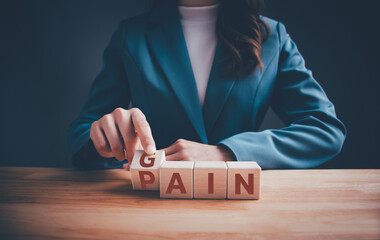 Businesswoman in green suit hand flipping wooden blocks cubes text between "PAIN" to "GAIN". Mindset for career growth business, motivation, aspiration, goal achievement management and change concept