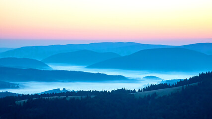 Fototapeta premium Colorful clouds in the sky at sunset against the backdrop of a mountainous forest area.
