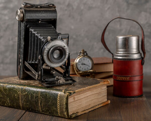 Antique bellows camera on an antique book with a thermos of coffee and a pocket watch next to it