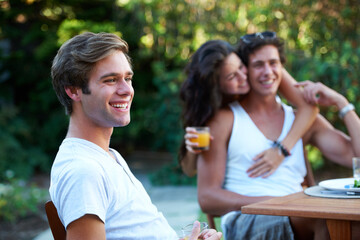 Young man, laughing and friends in a backyard at home with bbq and happy event by a table. Group,...