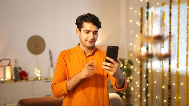 Indian handsome man wearing traditional dress waving and chatting on mobile phone during diwali festival.he is looking very good in yellow kurta,hindu festival.