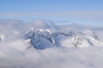 Breathtaking aerial view of alpine snowcapped mountain range peaking through heavy clouds. Mountain peaks of the Ötztal Alps from above. The impressive winter view is taken from an airplane window.