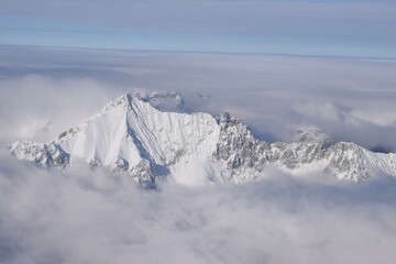 Breathtaking aerial view of alpine snowcapped mountain range peaking through heavy clouds. Mountain...