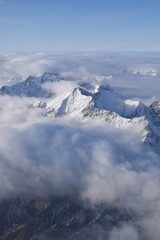 Fototapeta na wymiar Breathtaking aerial view of alpine snowcapped mountain range peaking through heavy clouds. Mountain peaks of the Ötztal Alps from above. The impressive winter view is taken from an airplane window.