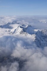 Breathtaking aerial view of alpine snowcapped mountain range peaking through heavy clouds. Mountain peaks of the Ötztal Alps from above. The impressive winter view is taken from an airplane window.