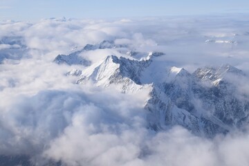 Breathtaking aerial view of alpine snowcapped mountain range peaking through heavy clouds. Mountain peaks of the Ötztal Alps from above. The impressive winter view is taken from an airplane window.