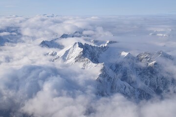 Breathtaking aerial view of alpine snowcapped mountain range peaking through heavy clouds. Mountain...