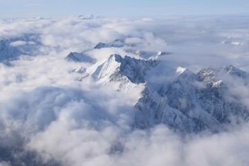 Fototapeta na wymiar Breathtaking aerial view of alpine snowcapped mountain range peaking through heavy clouds. Mountain peaks of the Ötztal Alps from above. The impressive winter view is taken from an airplane window.