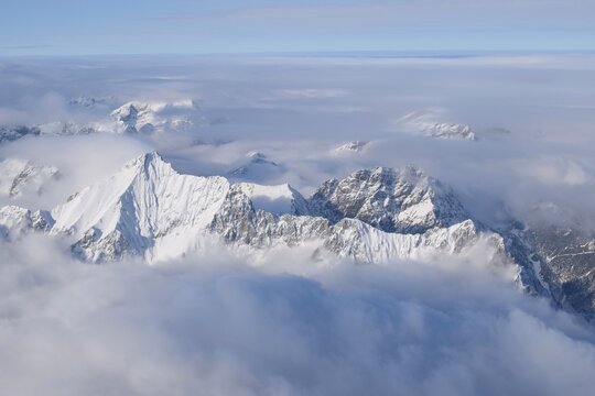 Breathtaking aerial view of alpine snowcapped mountain range peaking through heavy clouds. Mountain peaks of the Ötztal Alps from above. The impressive winter view is taken from an airplane window.