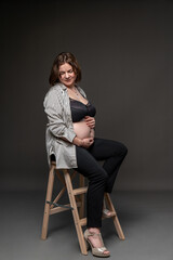 Portrait of a pregnant girl with a naked belly. Studio shooting. A woman sits on a chair, gray...