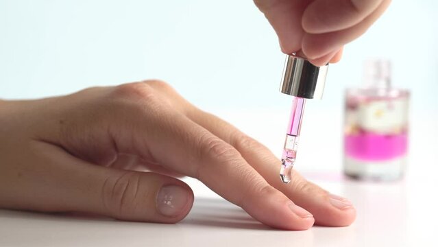 Moisturizing oil for cuticles. The woman cares for hands and nails, close up. Woman applying oil from pipette to cuticle on light background, macro. Healthy nails concept.