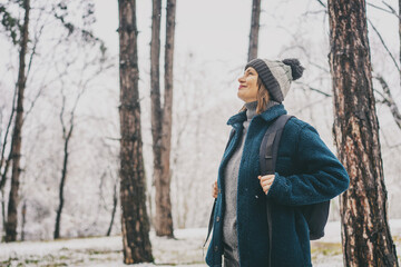 Adult mature woman breathes fresh air and enjoys the snowfall in the winter forest