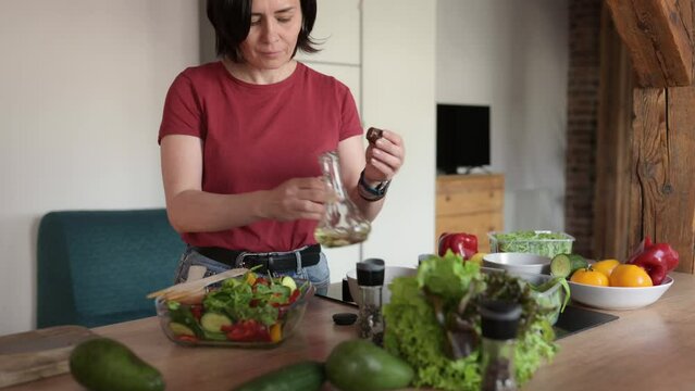 young woman cooking a healthy vegetable salad in the home kitchen, adding a healthy olive oil
