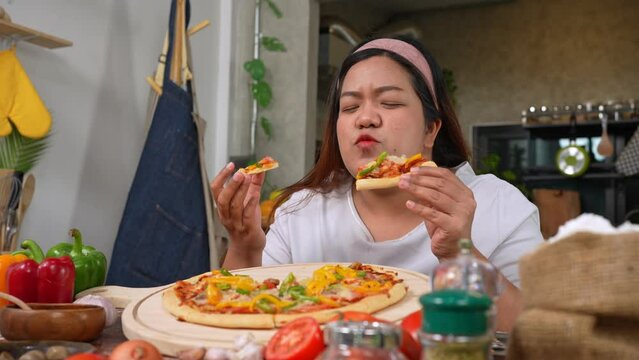 Happy Asian woman eating homemade pizza in home after baked pizza. Overweight women enjoy eating. Concept of binge eating disorder BED and Relaxing with Eating junk food and unhealthy foods.