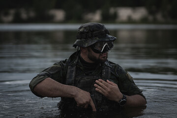 A military man, a combat swimmer, wearing a Panama hat, takes a pistol out of a holster in the water.