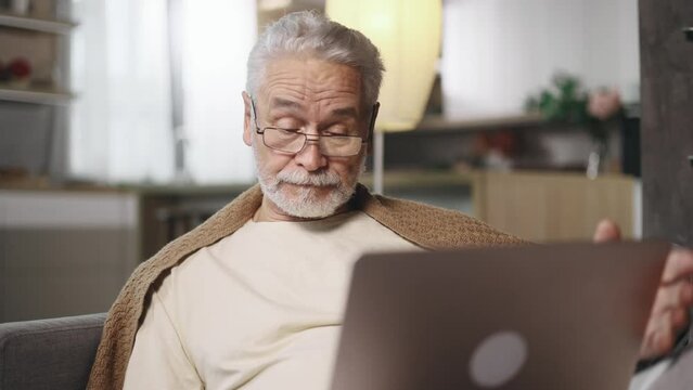 Sad grey haired senior man or freelancer with lack of new ideas or creative block typing and deleting text on laptop computer at home Worried male changing mind every few seconds indoors