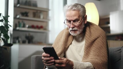 Sick grey haired senior man under the blanket coughing sneezing and having severe headache temperature when mentioned useful medical app service or site at home Cold and fever help service concept