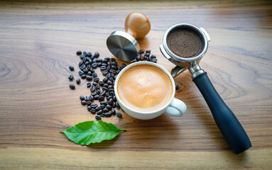Top view of Espresso coffee cup and equipment of barista coffee tool portafilter with tamper and dark roasted coffee beans with green coffee leaf  on wooden table