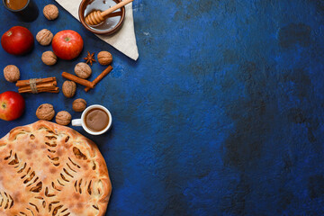 Whole apple pie for autumn coffee break. Bakery food, fresh red apples, cinnamon, espresso cup, honey in bowl on blue concrete table background. Traditional seasonal dessert, autumn harvest flat lay