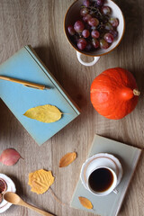 Cup of tea or coffee, plate with cookies and chocolate, dried oranges, bowl of grapes, vintage books, pumpkins and autumn leaves on the table. Autumnal hygge. Top view.