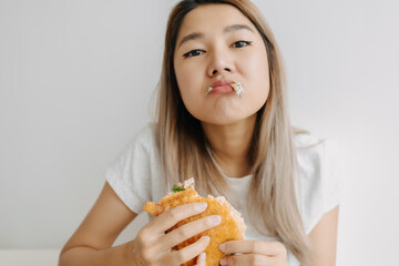 Asian Thai woman having homemade breakfast, eating sandwich hungrily at home alone.