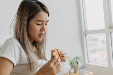 Asian Thai woman having homemade breakfast, eating sandwich hungrily at home alone.