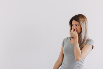 Unhappy Asian Thai woman wear grey, squeezing, pinching and holding nose, blocking bad smell, looking at empty space smelly, isolated on white background wall.
