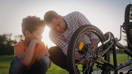 Multiracial dad teaching son how to repair wheel on bicycle