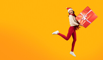 Woman With Large Present Box Jumping Over Yellow Studio Background
