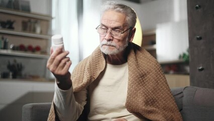Close up portrait of gray haired senior man reading medical instructions or composition of drug before taking medicine at home Focused male checking pills for ingredients and information indoors