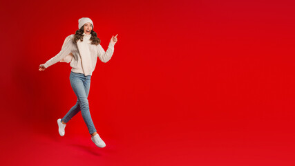 Excited Woman In Santa Hat Running Over Red Studio Background