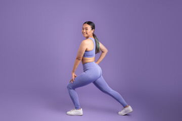Fototapeta na wymiar Japanese young woman stretching legs doing lunges on purple studio background