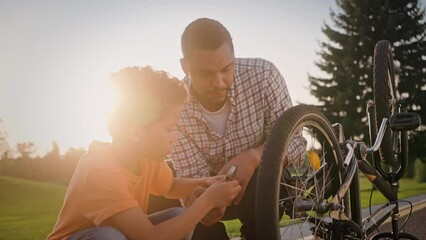 Caring father and son fixing bicycle wheel at park