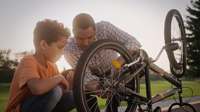 Dad and son trying to fix broken wheel of bike outdoors