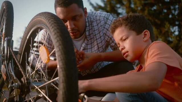 Father with son using wrench for fixing bicycle wheel