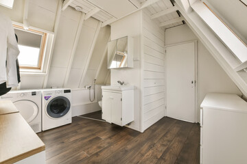 a laundry room with wood flooring and white washer in the space is located on top of an attic loft