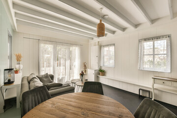 a living room with white walls and wood table in the center of the room there is a large window that looks out onto the