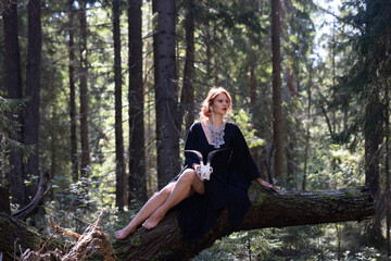 Fototapeta premium Red-haired sorceress resting in the forest on a log