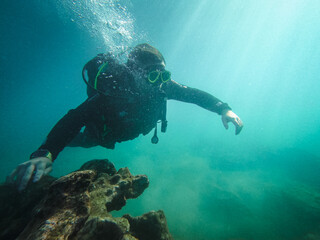 A man in a black wetsuit is diving underwater, exploring the ocean floor.